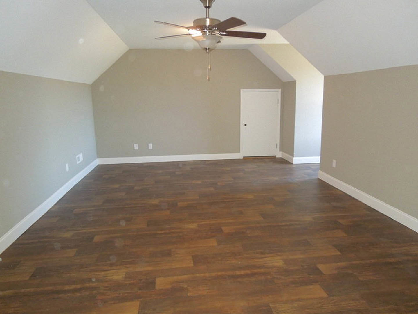 Ceiling fan with light fixture above wood laminate flooring, white walls, and a white door featuring a round hole