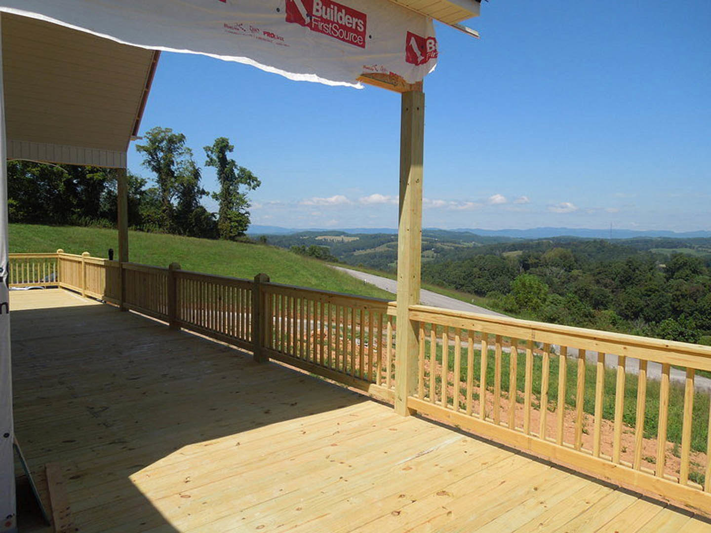 Wooden deck with horizontal fence, green hill and trees in background, red and white sign attached to fence
