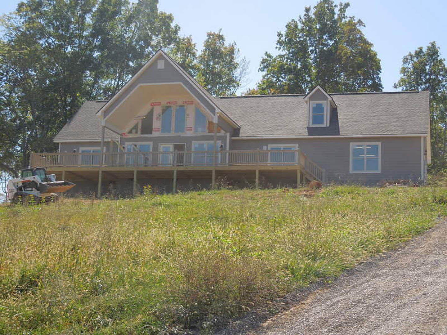 Two-story house with white siding, covered front porch, concrete driveway, manicured lawn, and mature trees in the background