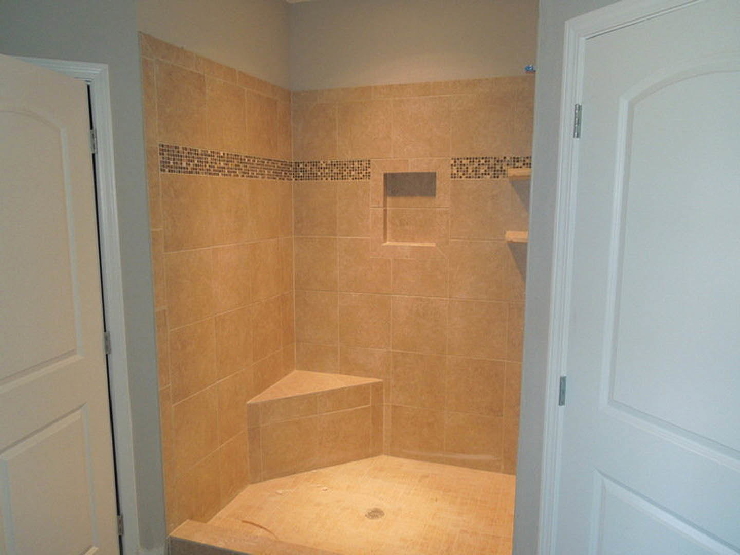 Walk-in shower with gray tile floor, built-in bench, recessed shelf, white door, and white wall detailing