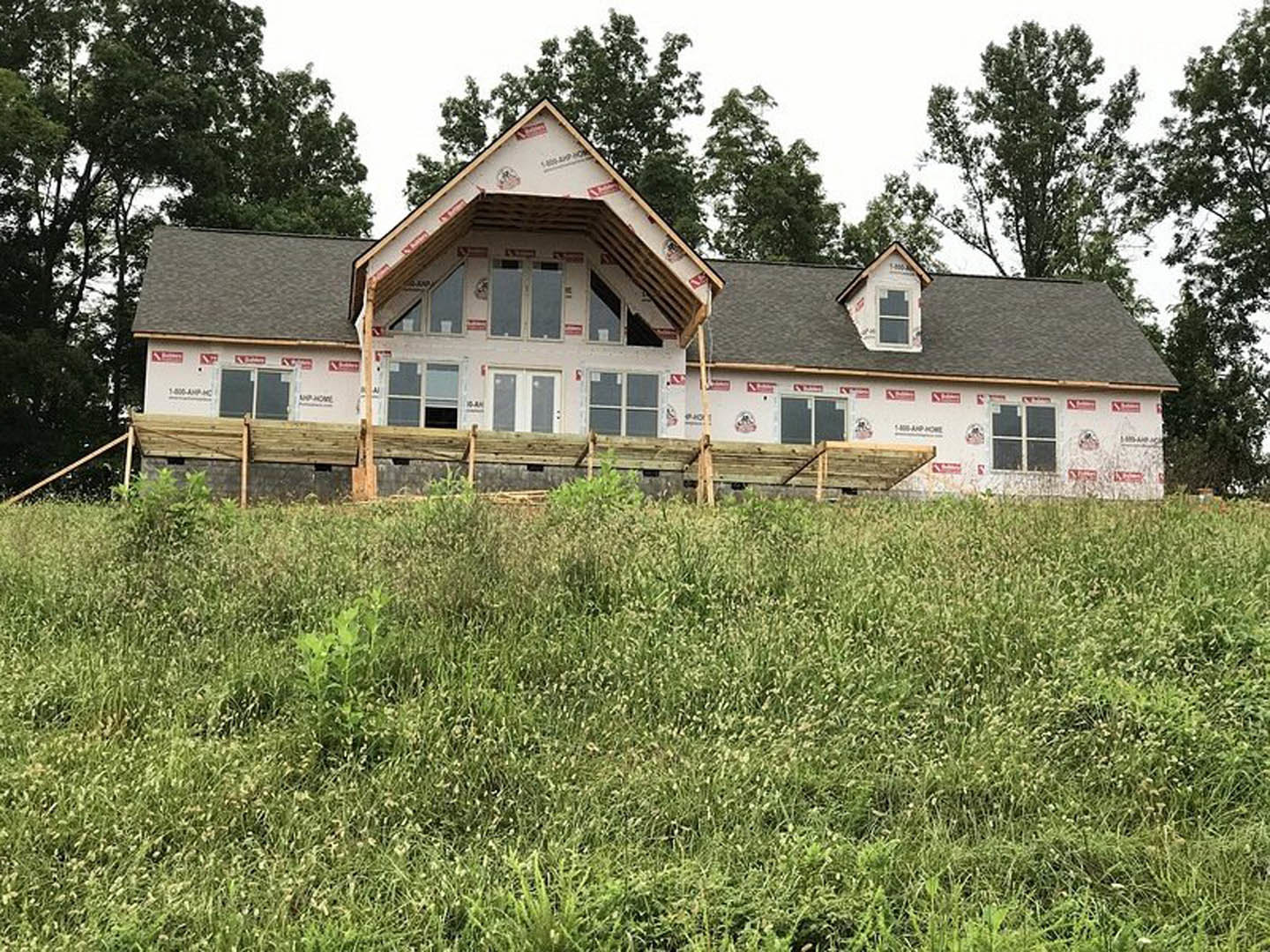 Two-story farmhouse with white siding, black-framed windows, wooden fence, manicured lawn, and mature trees in the background