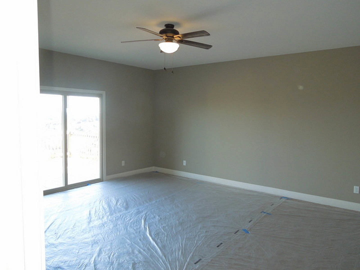 Spacious room with two ceiling fans, white walls, large window, light fixture, and white plastic floor covering