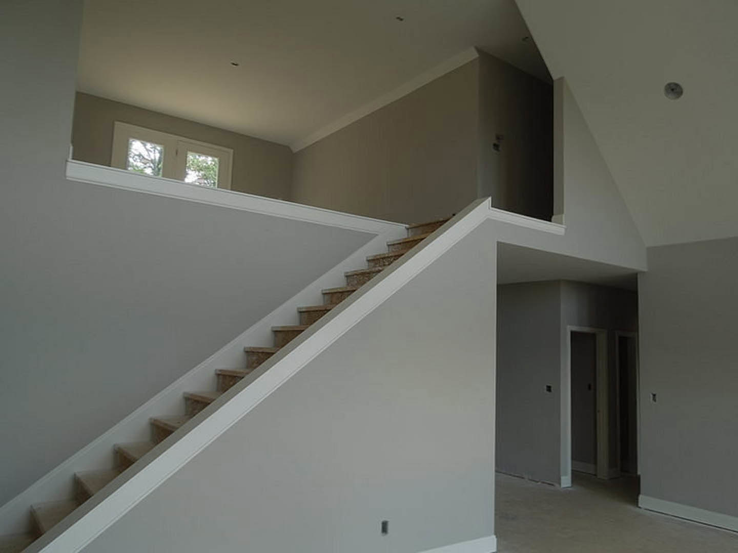 White staircase with wooden handrail, white plaster walls, square windows, white floor with matching trim, adjacent doorway leading to another room