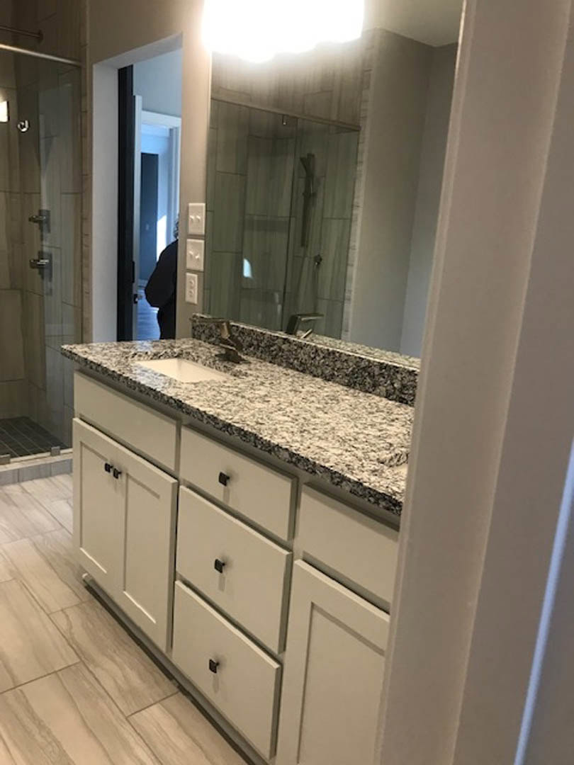 Bathroom featuring marble countertop with undermount sink, large wall mirror, white tile flooring, glass shower enclosure, chrome fixtures, and white cabinetry