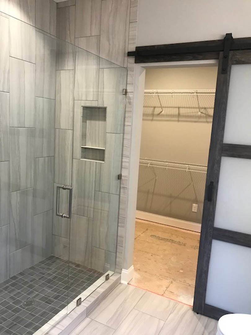 Modern bathroom featuring a frameless glass shower door, white tile walls, black hardware, and light tile flooring