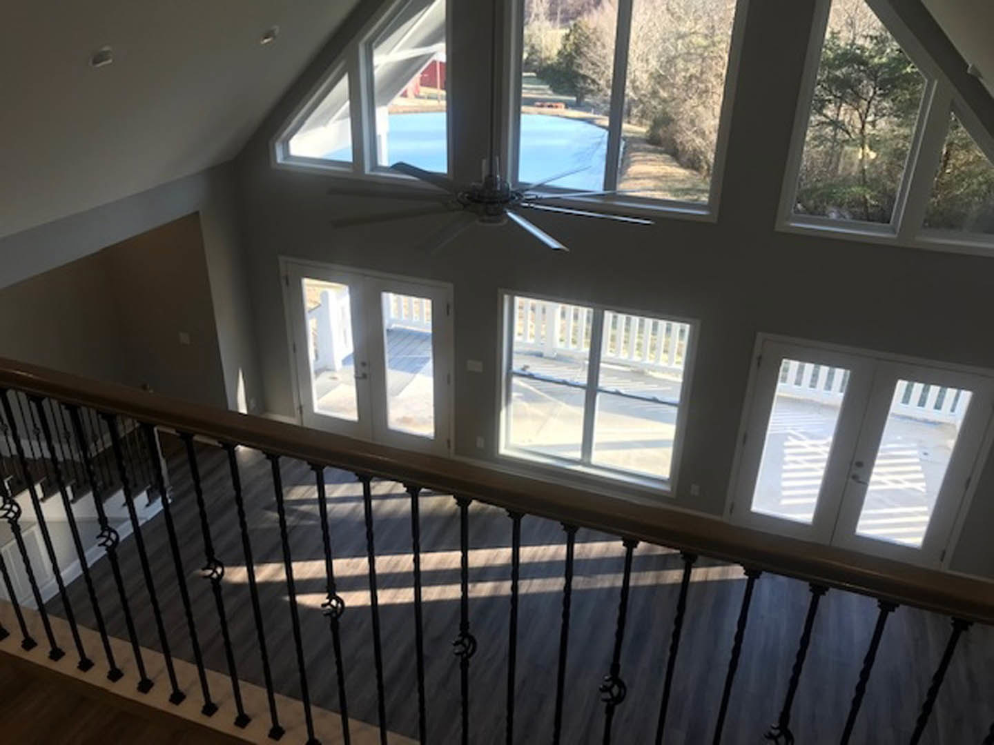 Top-down view of staircase with white railing, wood flooring, large windows overlooking lake and trees, ceiling fan, and glass door leading to balcony.