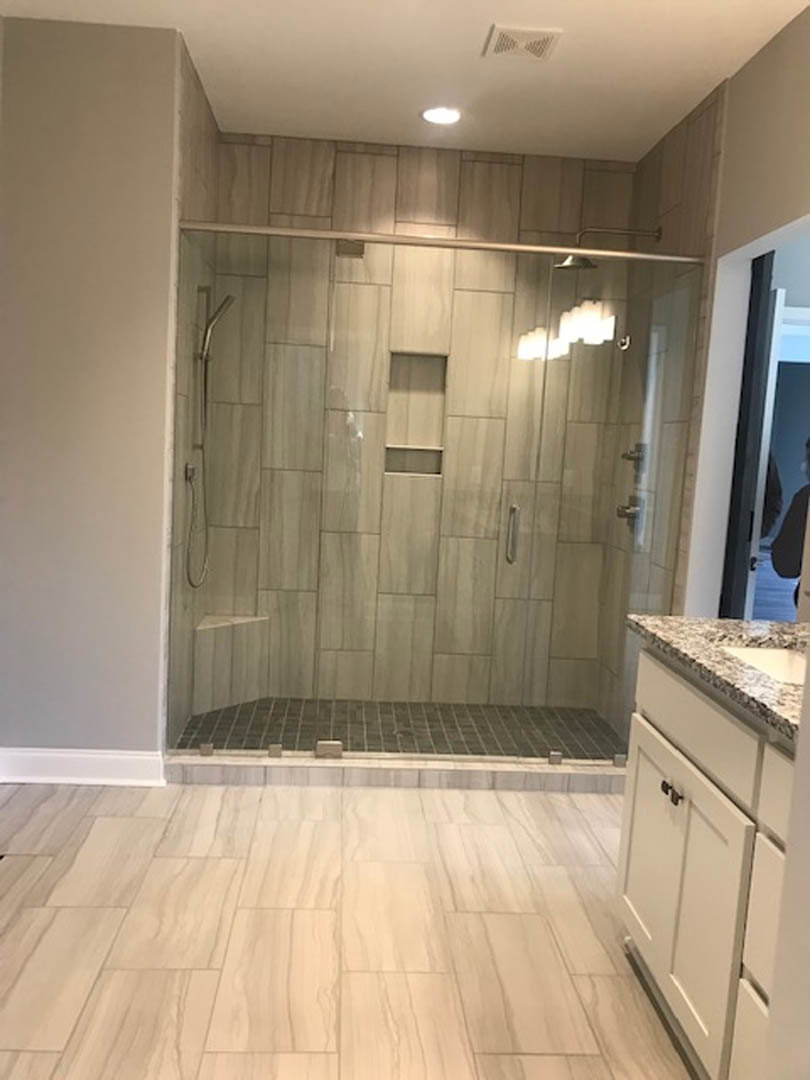 Bathroom featuring a glass shower enclosure, white cabinetry with black handles, tile flooring, and partial view of a light fixture.