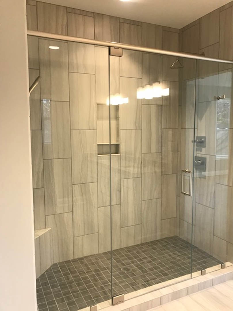 Glass shower enclosure with silver handle, white tile walls, and tile flooring in a modern bathroom.