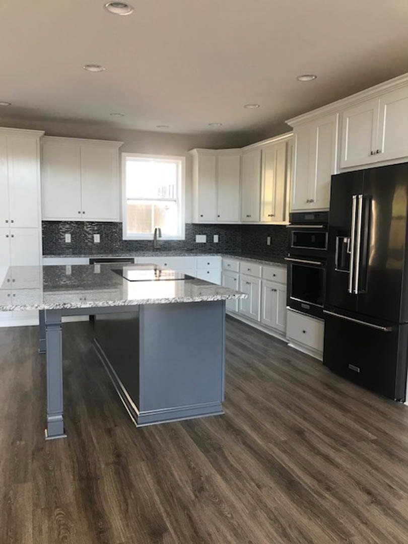 Marble kitchen island with waterfall edge, wood flooring, black refrigerator and oven, white cabinetry, window with natural light, stainless steel sink