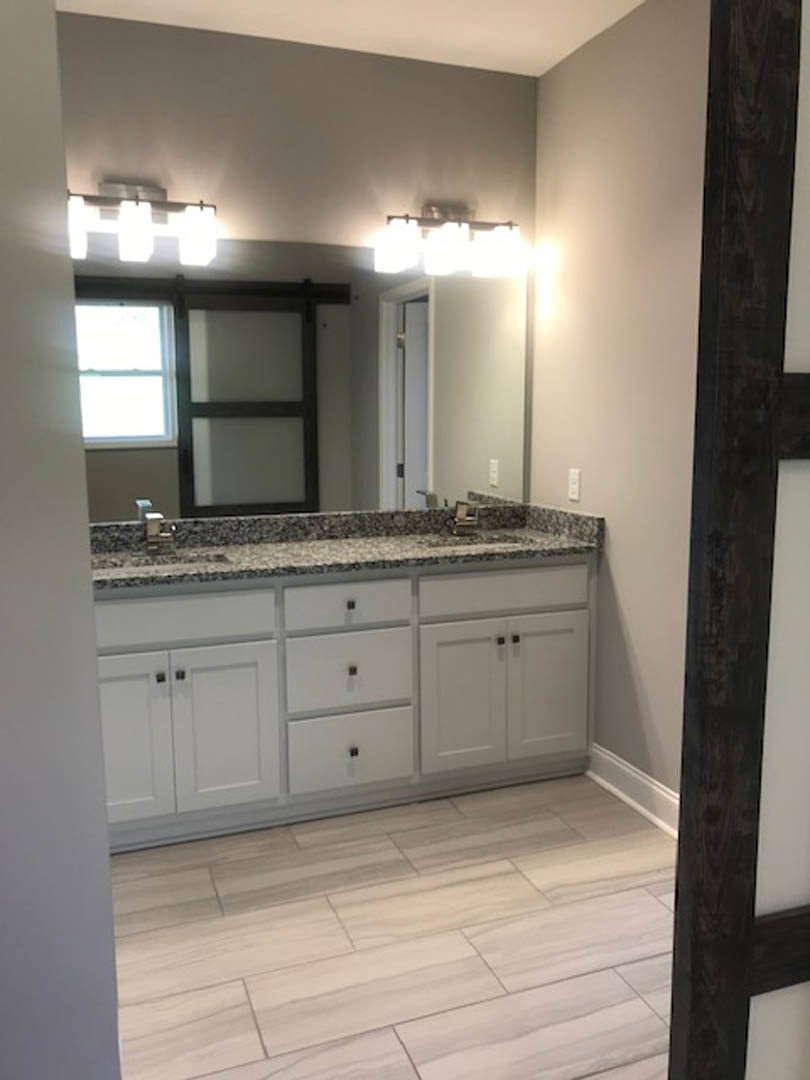 Marble bathroom countertop with undermount sink, large framed mirror above, white cabinetry, chrome faucet, tile flooring, and wall-mounted light fixtures
