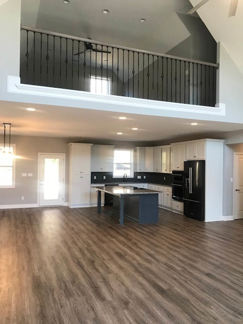 Open-concept kitchen and living room featuring black cabinets with silver handles, marble-topped table, wood flooring, black countertop, white door illuminated by natural light