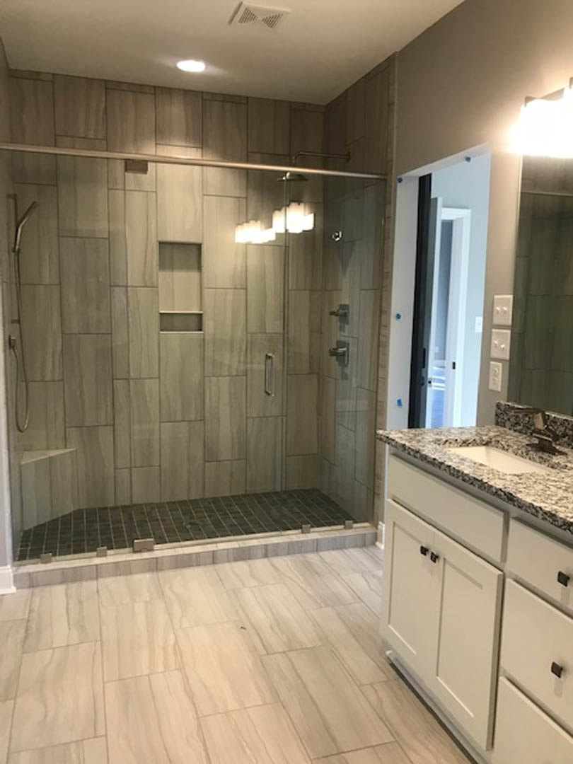 Bathroom with glass shower enclosure, white tile floor with border, white cabinet, and countertop-mounted sink with chrome faucet