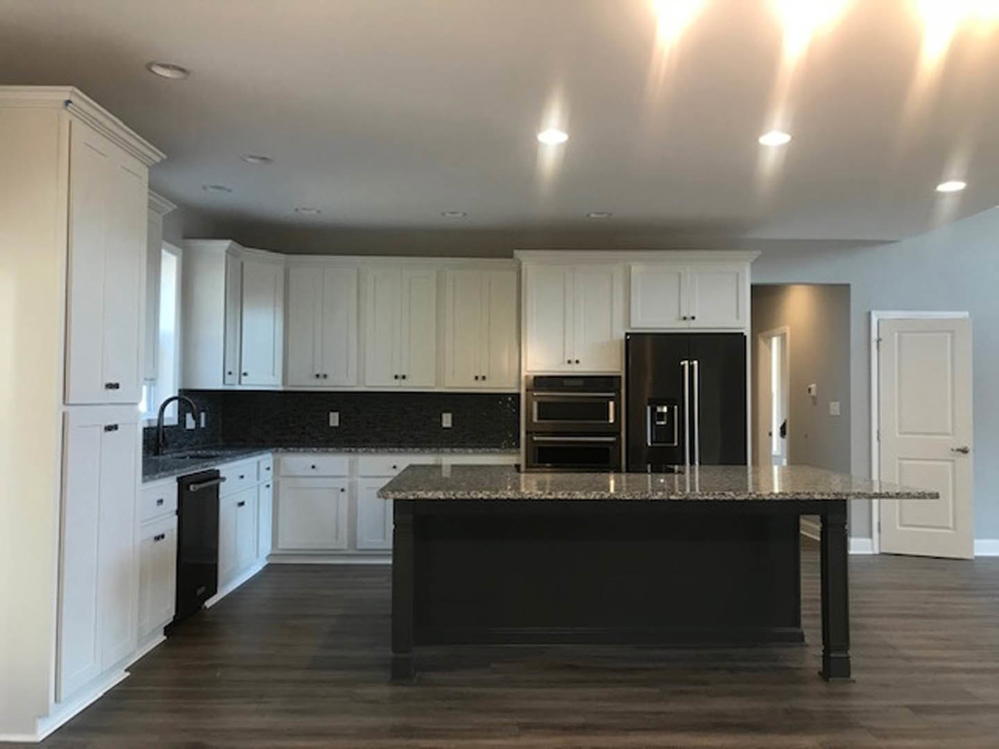 Spacious kitchen featuring a large marbled black island countertop, black refrigerator with silver handles, white cabinetry, built-in microwave, and a white door with a silver