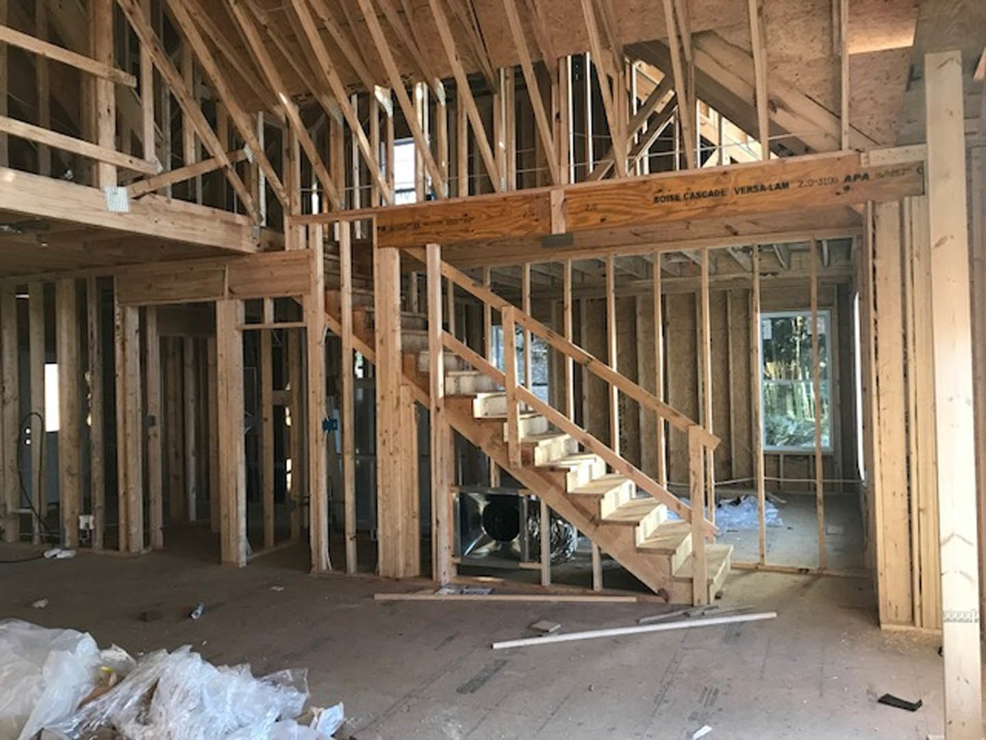 Exposed wood framing and beams inside a house under construction, with unfinished wooden staircase and visible insulation