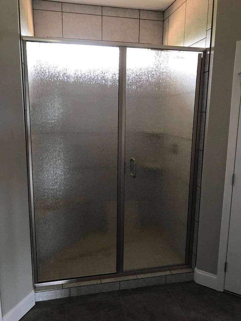 Shower enclosure with frosted glass doors, black tile floor bordered in white, grey door and window visible in modern bathroom interior