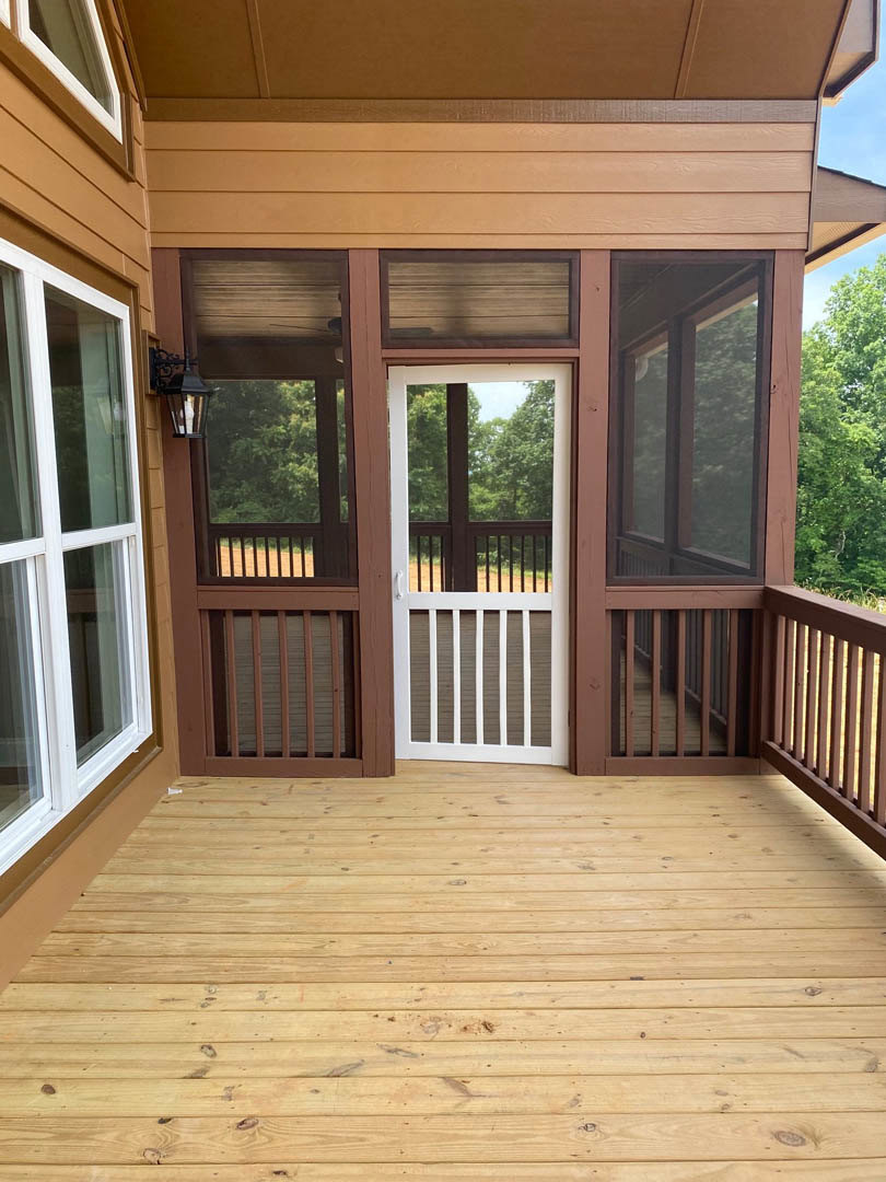 Wooden porch with white railing and door, brown siding with white trim, window showing tree view