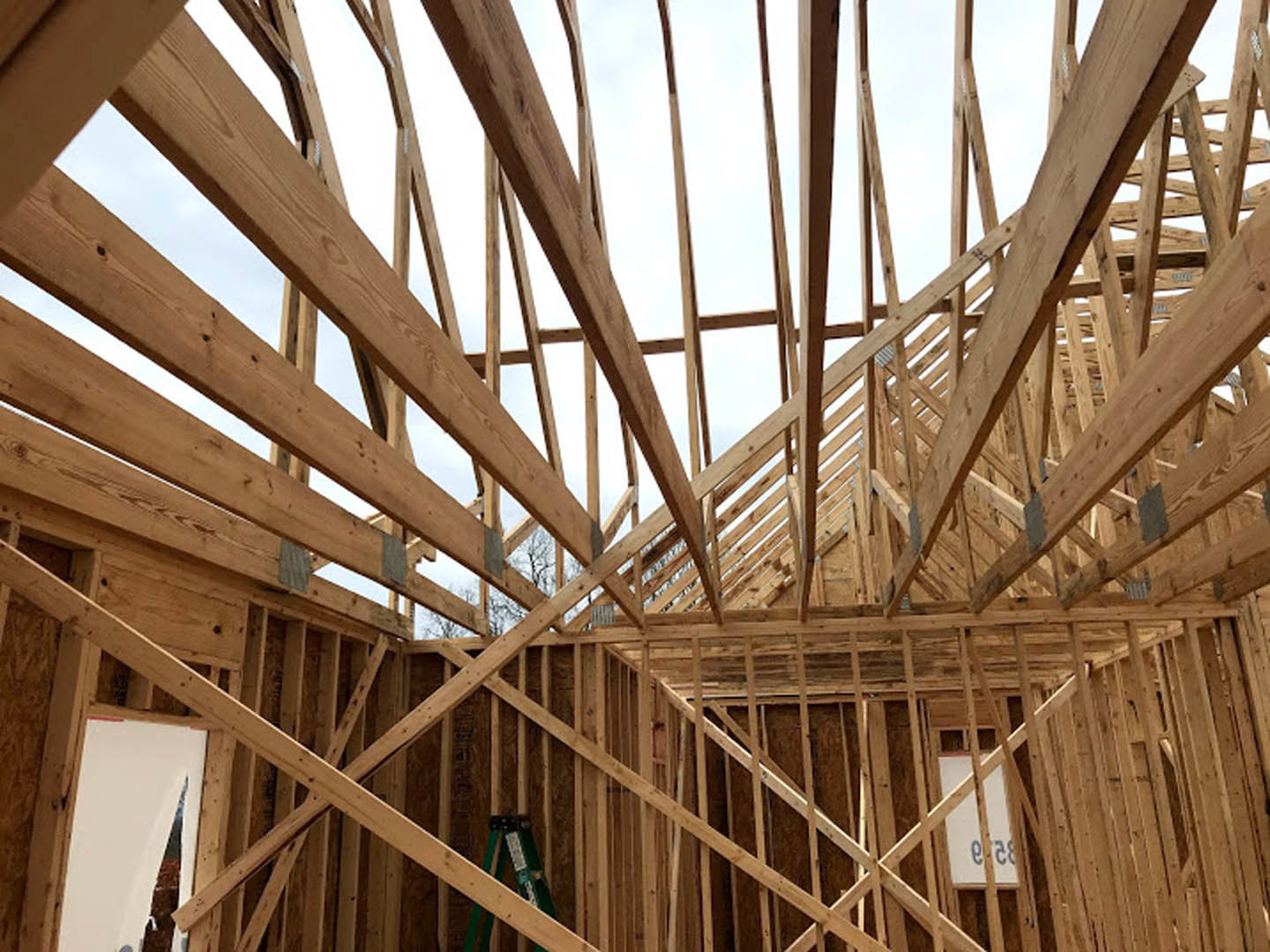 Exposed wood framing structure of a custom home under construction with beams and lumber against a clear sky