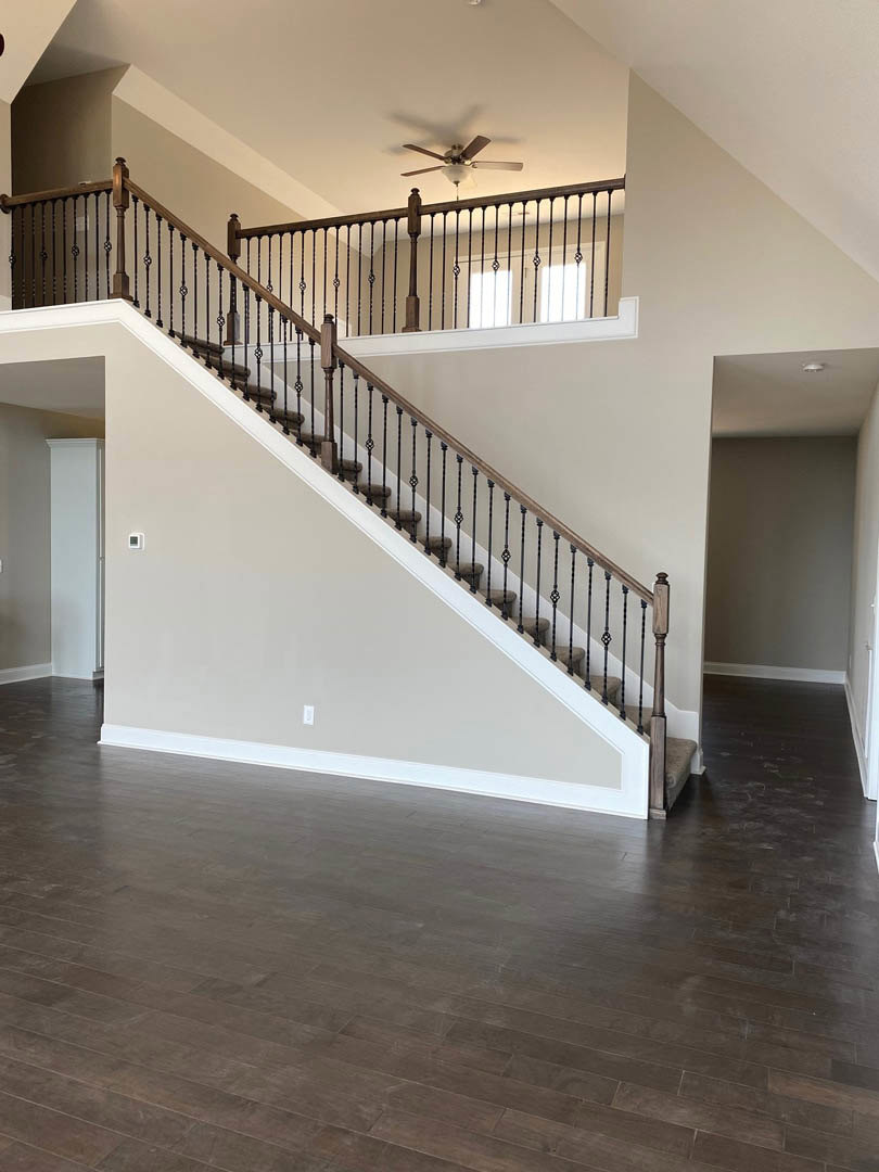 Hardwood staircase with black metal railings, white walls with black trim, ceiling fan and light fixture, sunlight streaming through window onto wood flooring