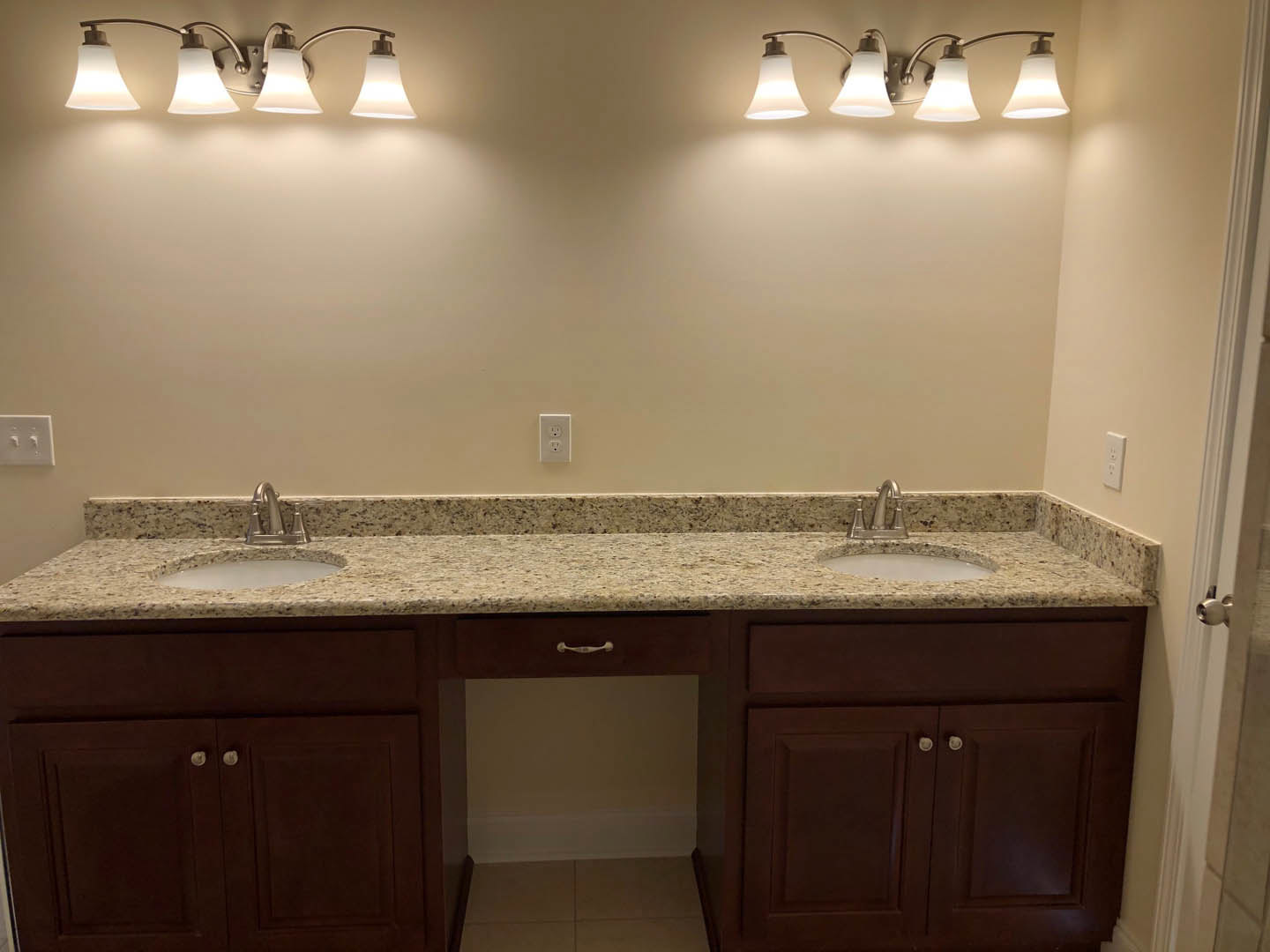 Bathroom with double sinks, marbled countertop, white cabinetry, and two modern light fixtures above mirrors