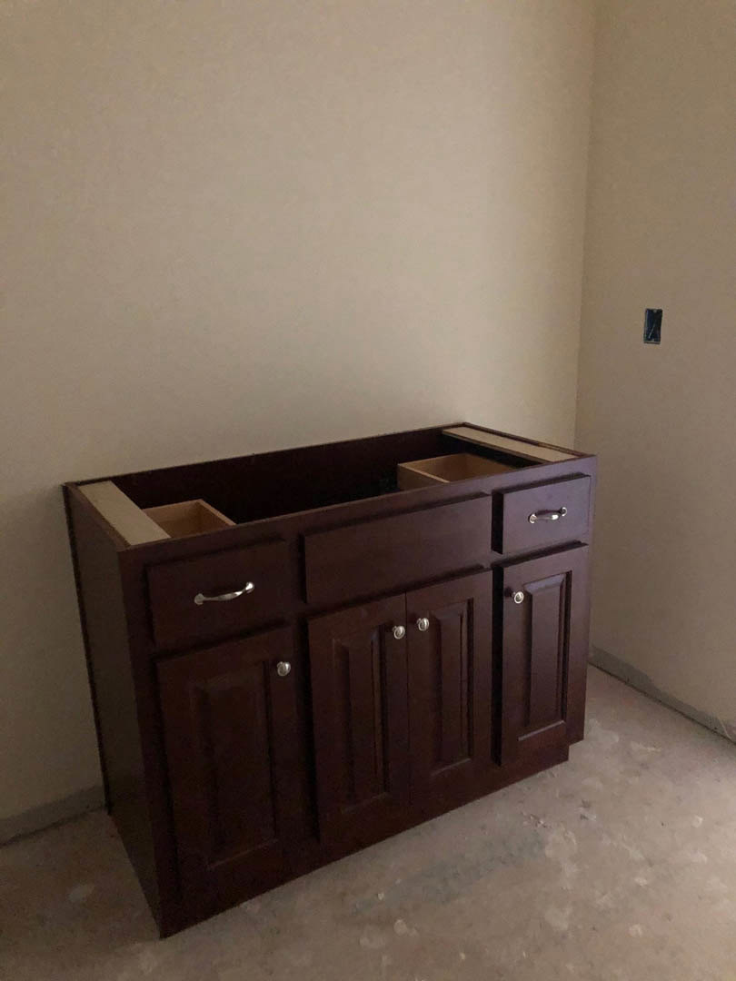 Brown wooden kitchen cabinet with multiple drawers, silver handles, and smooth finish, set against a tiled floor