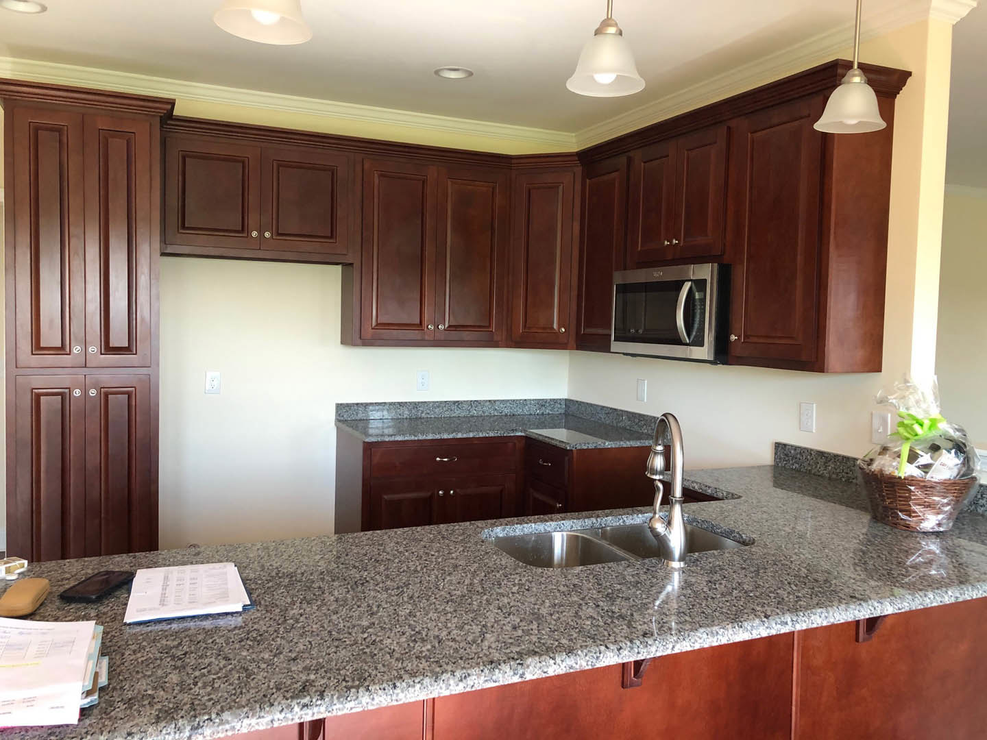 Granite kitchen countertops with white cabinetry, stainless steel microwave, sink, and basket of food on the counter