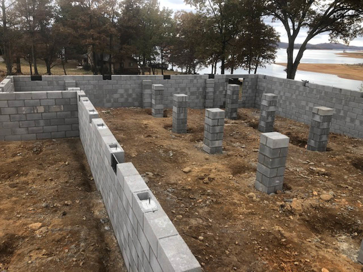 Concrete block wall and pillar under construction on a residential building site, surrounded by dirt ground and scattered bricks.