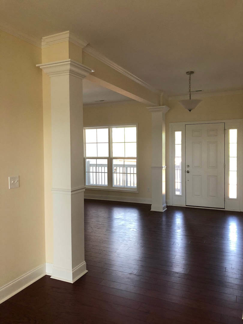 Hardwood floor with white pillars, white paneled door featuring glass inserts, light switch on plaster wall, window allowing natural light into the room