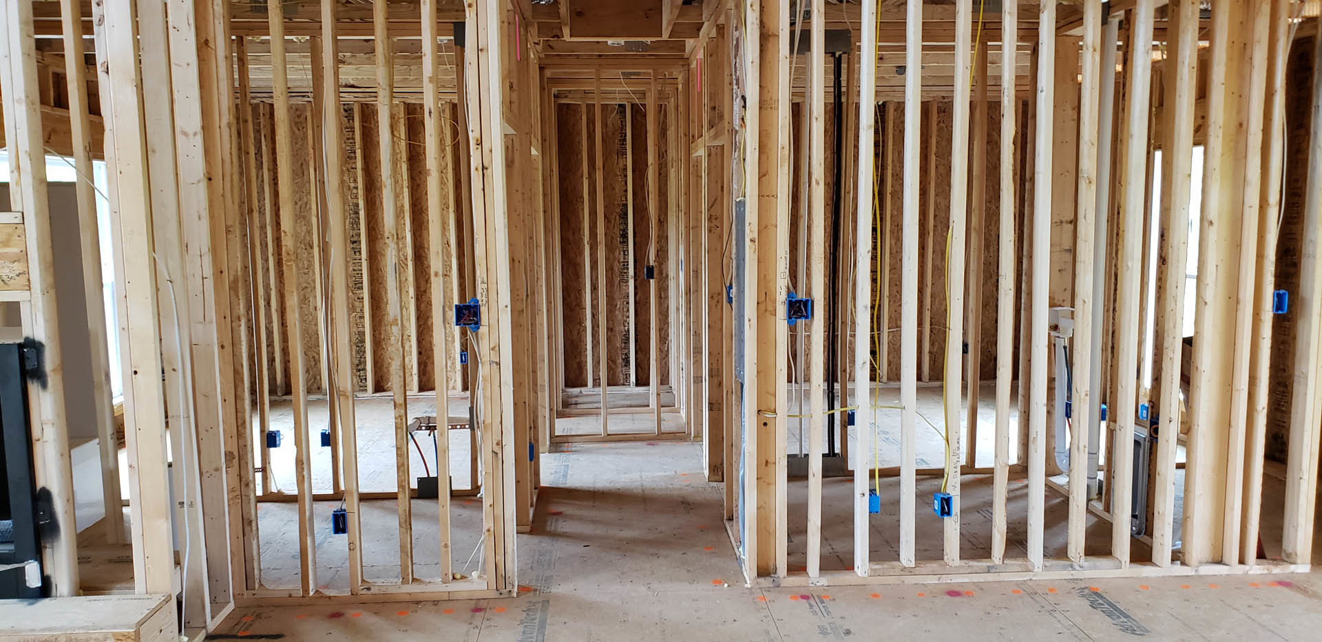 Unfinished room with exposed wood framing, electrical wiring, blue electrical boxes, and a partially visible person in the background