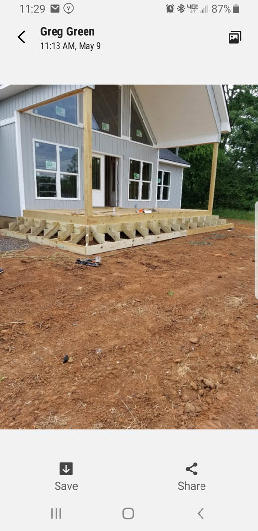 Wood-framed porch under construction attached to blue-sided house, exposed wooden platform with cutouts, close-up window, construction sign on exterior wall