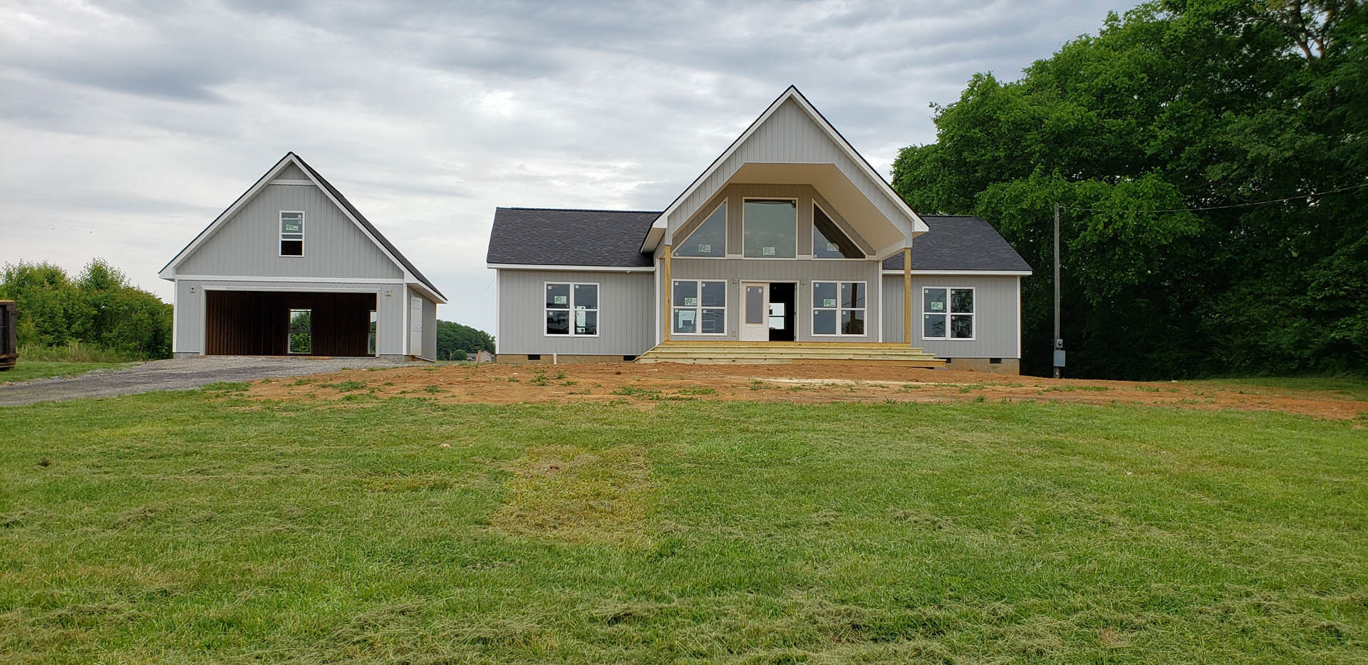 Two-story house with attached garage, green lawn in foreground, Robert Frost Farm visible in background, cloudy sky overhead