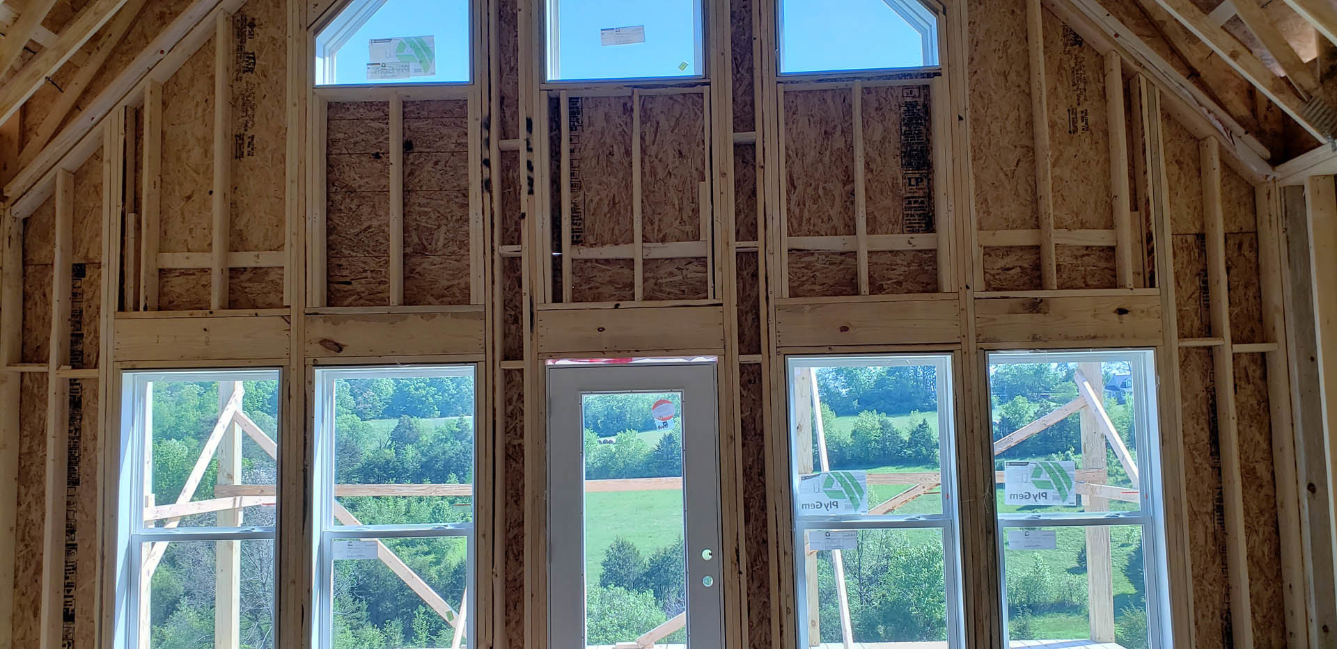 Exposed wood framing with installed windows and door opening, natural daylight highlighting unfinished lumber in residential construction
