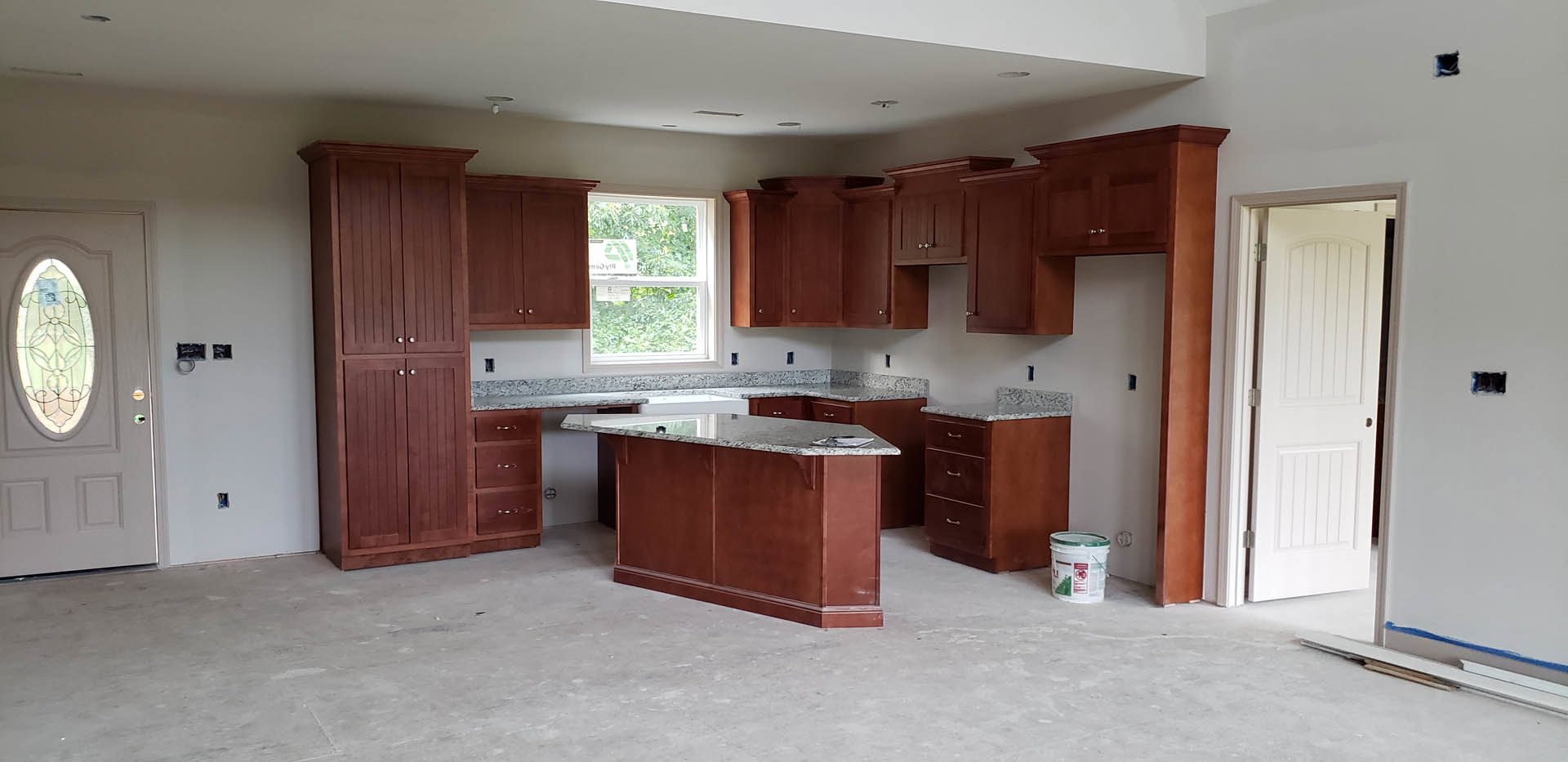 Marble-topped brown kitchen counter with white cabinetry, stainless sink, window with sign, and white door with silver doorknob