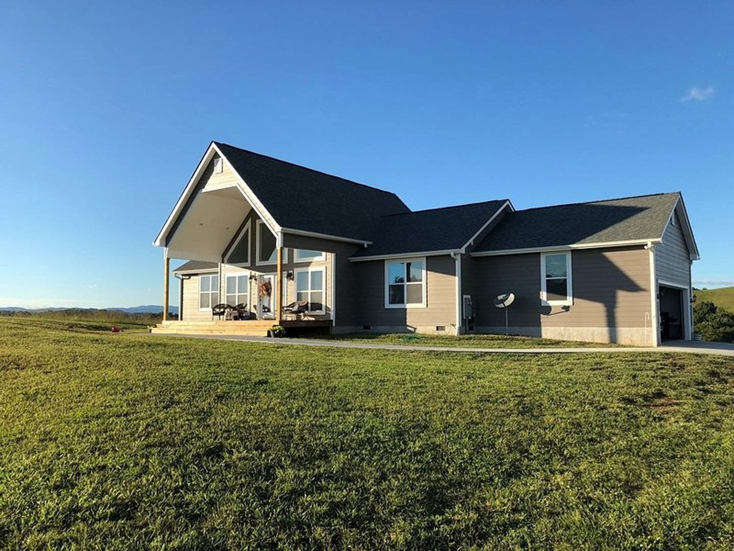 Two-story house with gray shingle roof, white-framed windows, and satellite dish, surrounded by green grass lawn and mature trees
