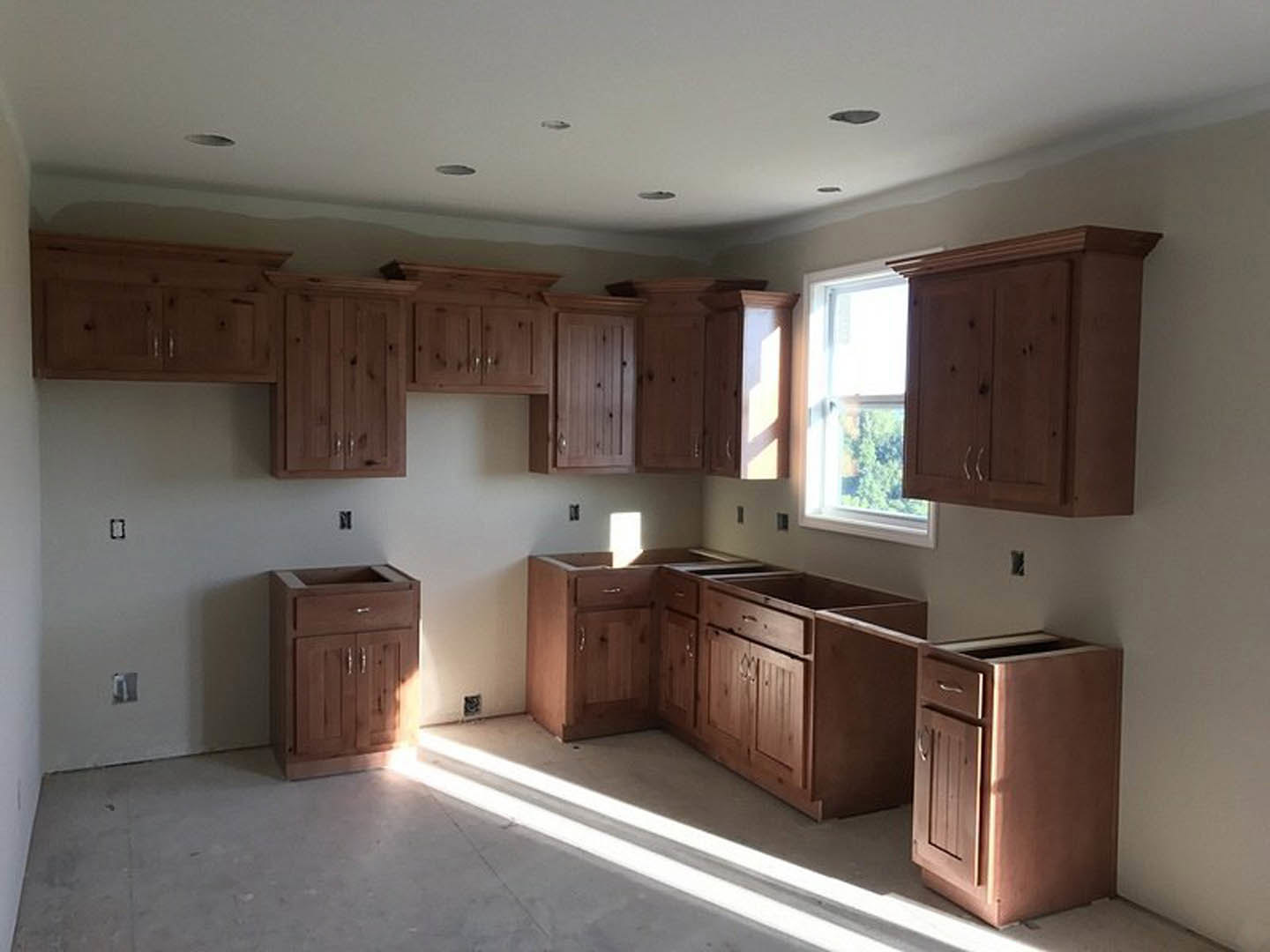 Kitchen with natural wood cabinets, stone countertop, stainless steel appliances, and a window overlooking leafy trees