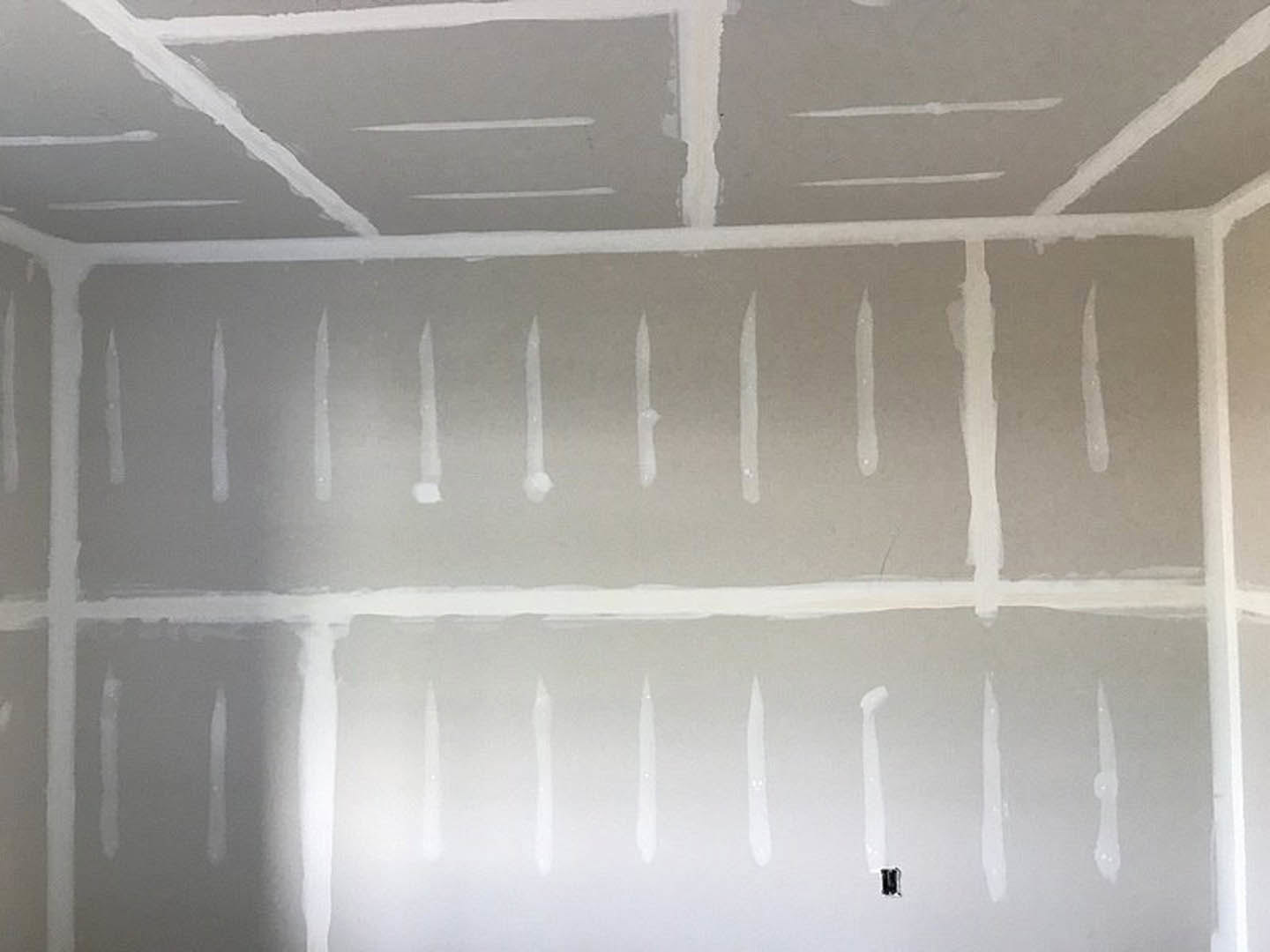 White painted drywall wall with subtle texture, white ceiling above featuring linear details, close-up of white paint dripping down wall surface.