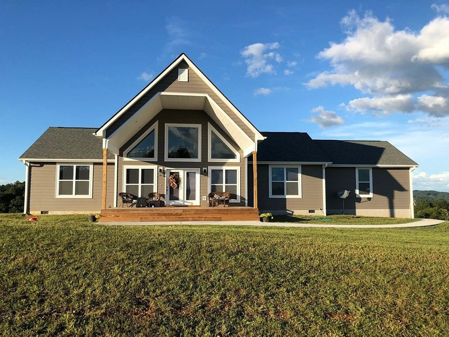 Two-story home with white-framed windows, wood porch, and manicured green lawn under a blue sky with scattered clouds