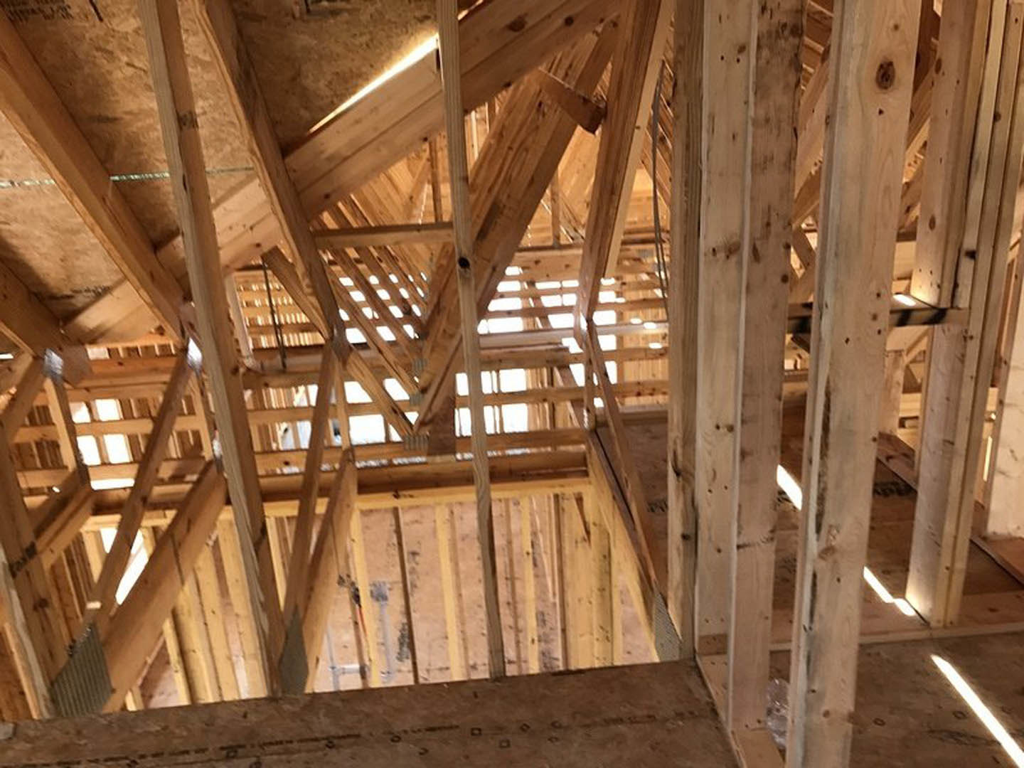 Exposed wood framing and beams forming the structure of a custom home under construction, with visible ceiling joists and unfinished lumber.
