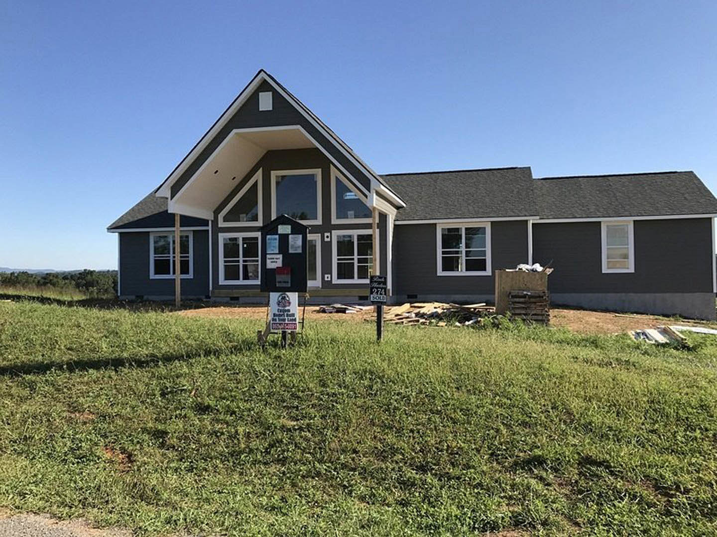 Two-story cottage with white siding, black-framed windows, grassy front yard, mailbox, and several real estate signs placed near the walkway.