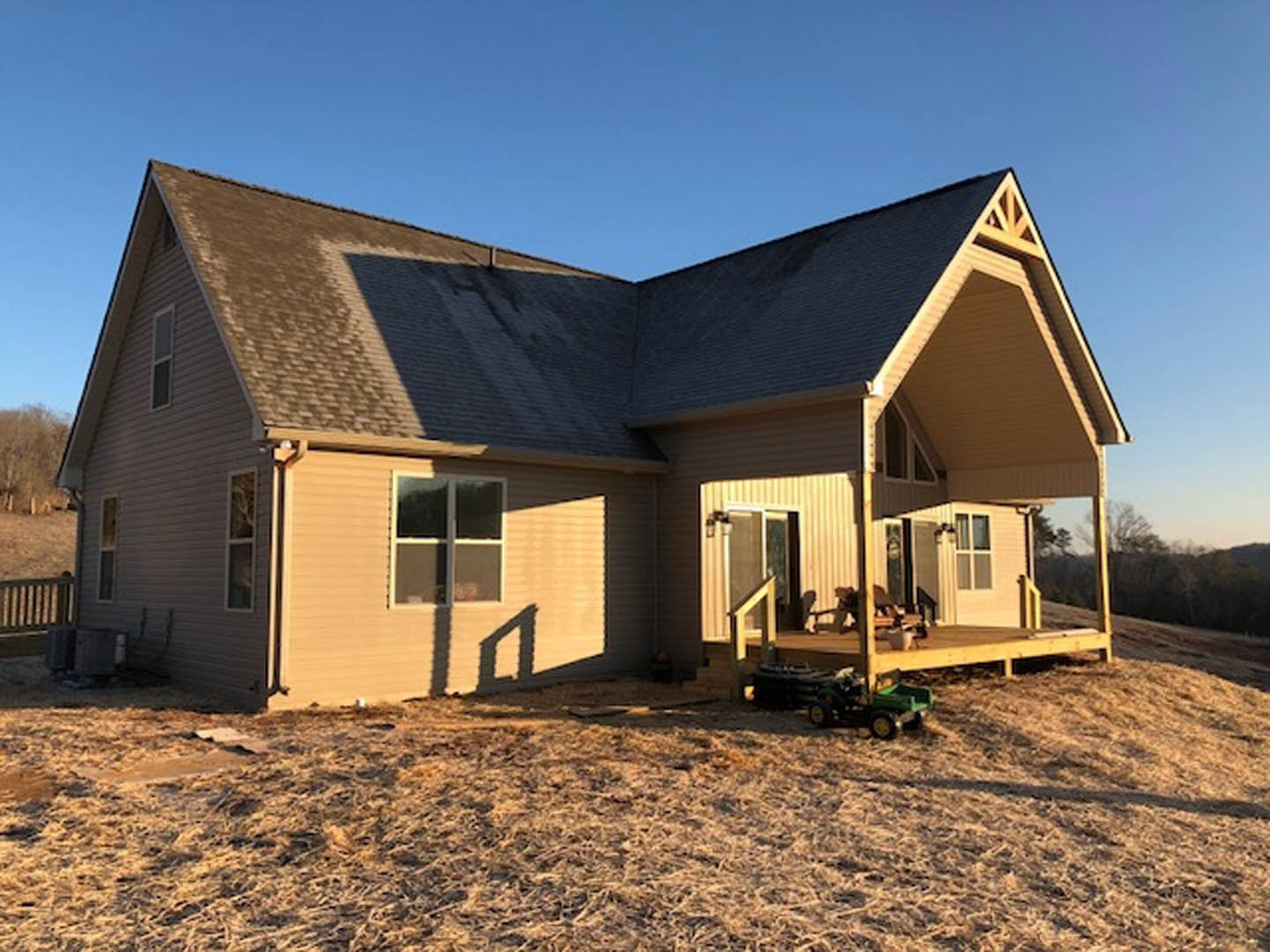 Two-story home with wood deck, white trim windows, green lawn, and lawnmower parked near the porch