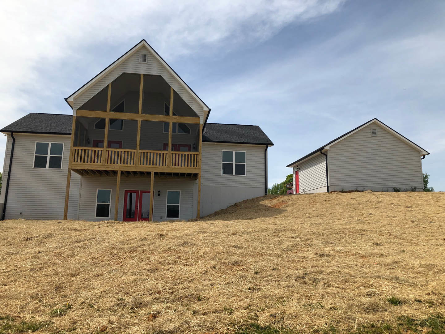 Two-story house with gray siding, covered front porch, attached garage, red front door with glass panels, white trim, windows, and grassy lawn under partly cloudy sky