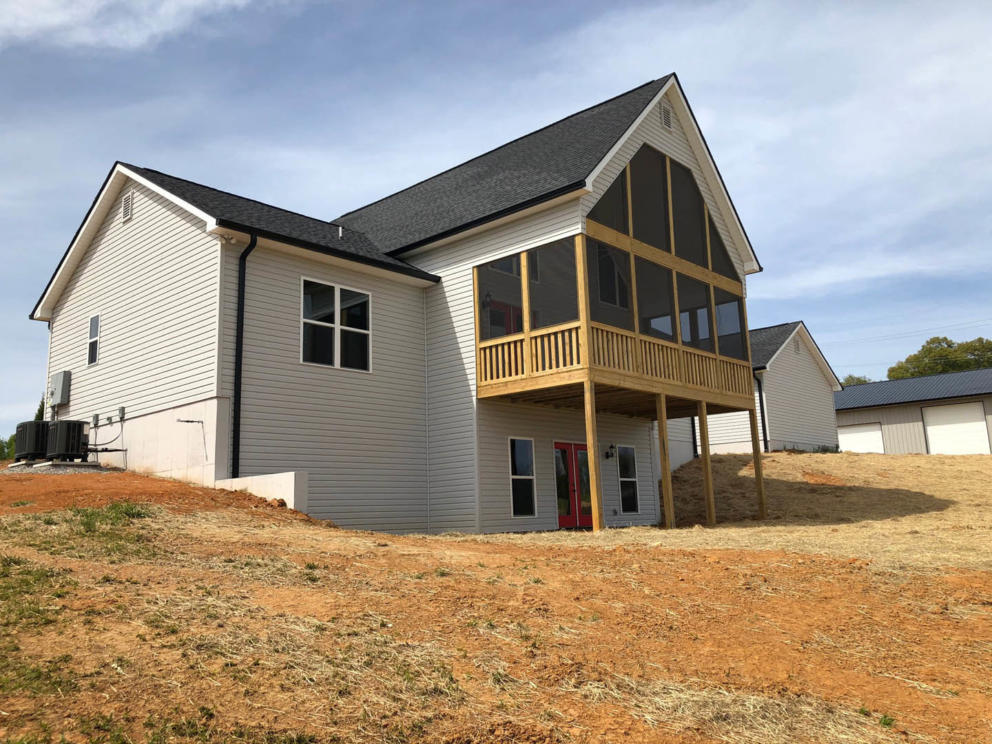 Two-story home with white siding, red front door and trim, covered porch with white columns, upper balcony, large windows with white frames, gabled roof, manicured lawn, and partly