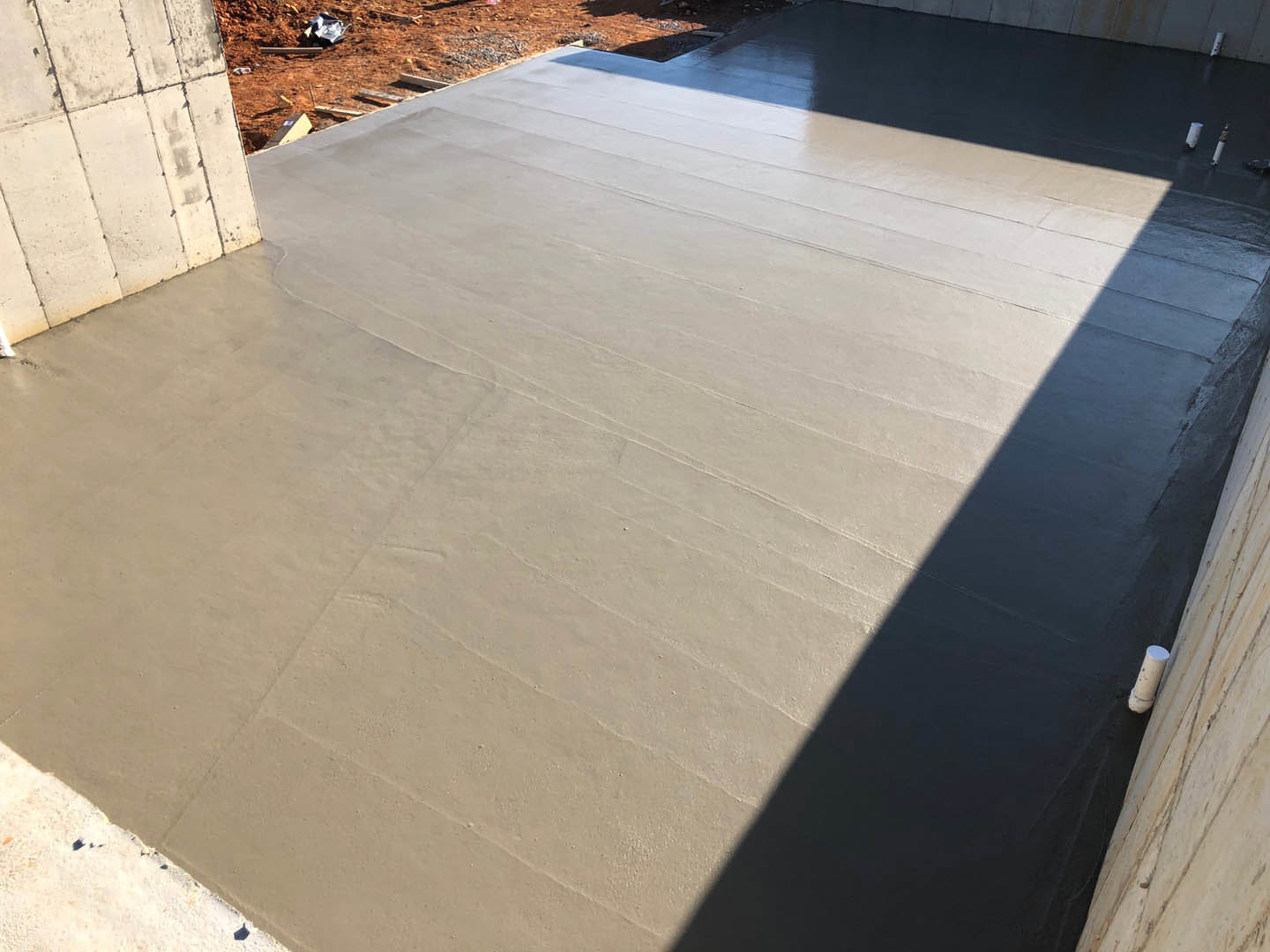 Concrete floor and cement wall with a white cylinder featuring black spots, adjacent to a road.