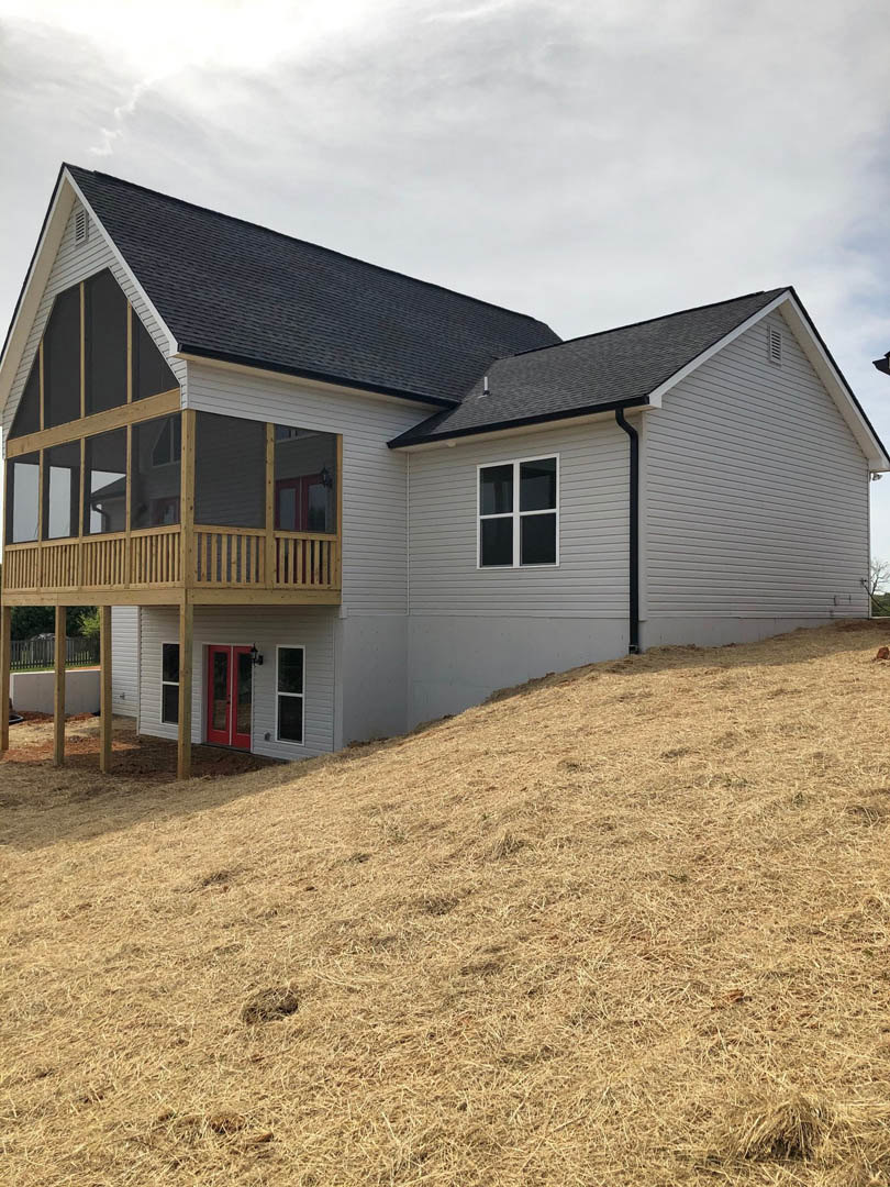 Two-story house with white siding, red front door, covered porch, white-framed windows, and grassy hill in front