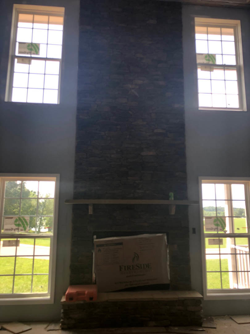 Stone fireplace with rectangular firebox, flanked by large multi-pane windows, in a bright living room with light-colored walls