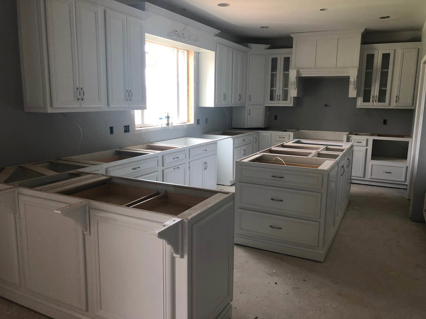 White kitchen cabinets and drawers with black handles, light streaming through window onto quartz countertops, stainless steel appliances, and neutral walls