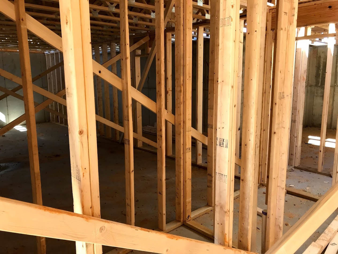 Exposed wooden framing and beams inside a partially constructed house, with natural light filtering through unfinished roof planks.