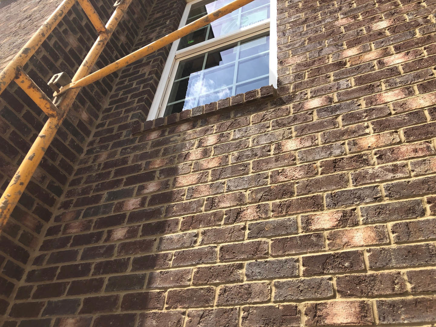 Red brick exterior wall with rectangular window and yellow pipe running vertically alongside window