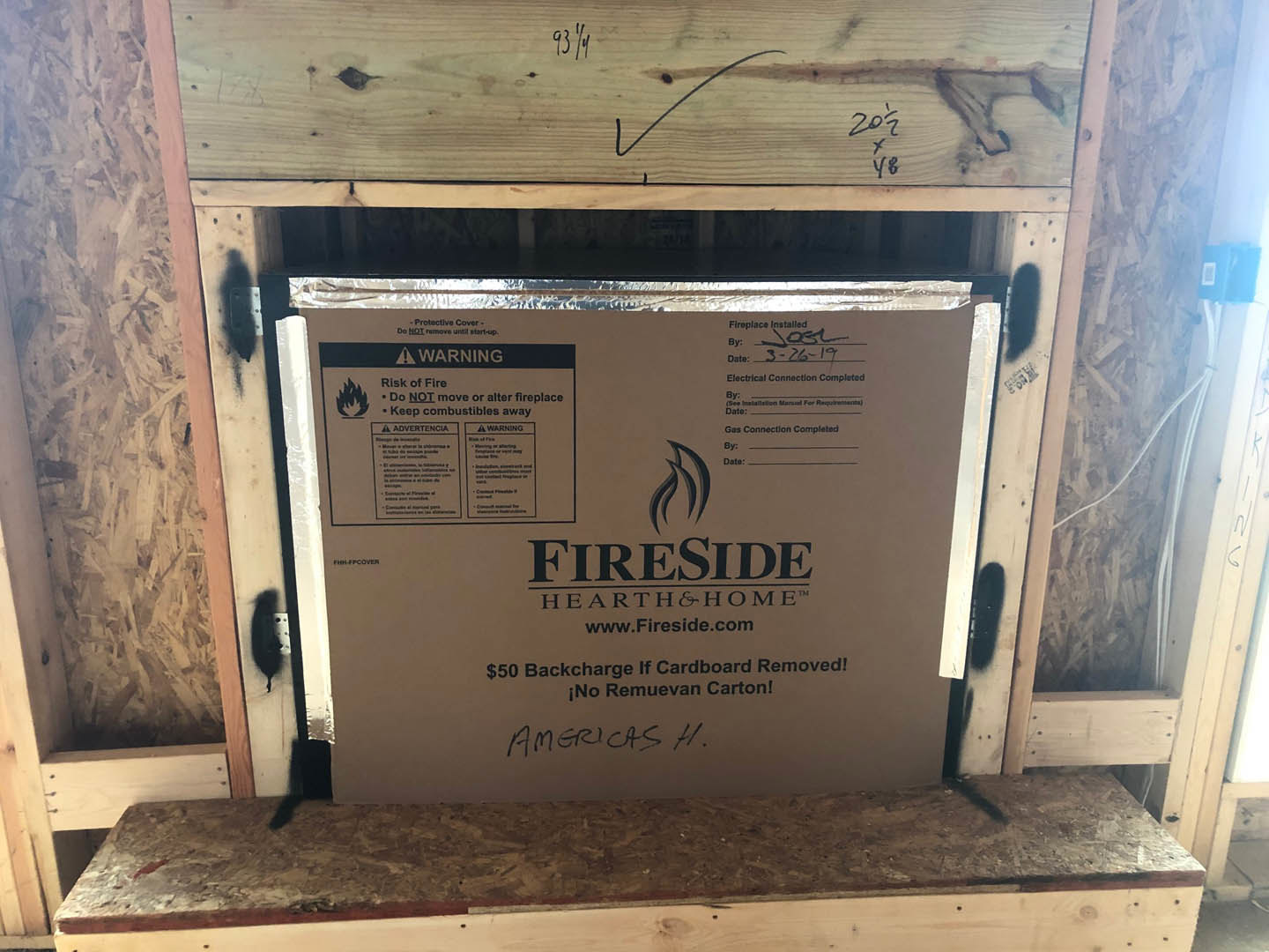 Cardboard box labeled "bartholomew" resting on unfinished wood framing near a partially constructed wall and fireplace.