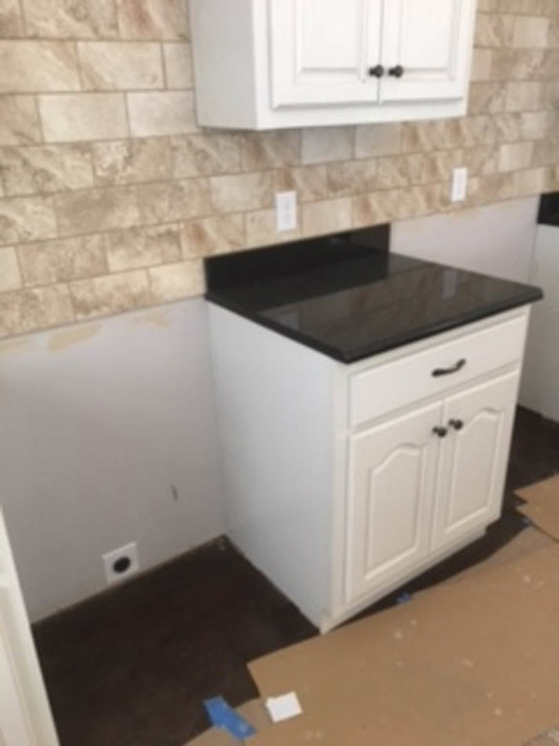 White cabinetry with matte black countertop, stainless steel sink and faucet, tile backsplash, and integrated drawers in a modern kitchen.
