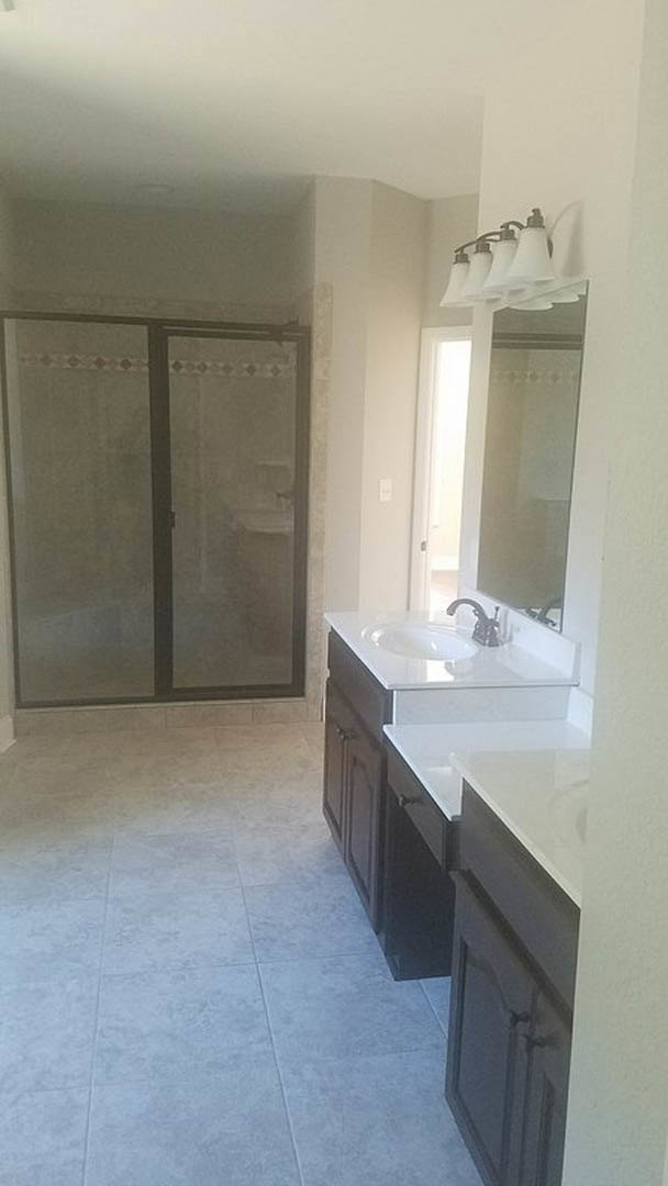 Modern bathroom featuring a glass-enclosed shower, white sink with chrome faucet, light wood cabinetry, stone countertop, and neutral tile flooring